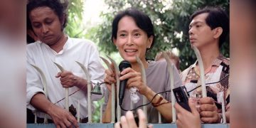 ၁၉၉၅ ခုနှစ်၊ ဇူလိုင်လ ၁၄ ရက်က ရန်ကုန်မြို့၊ တက္ကသိုလ်ရိပ်သာလမ်းရှိ နေအိမ်ရှေ့တွင် ထောက်ခံအား ပေးသူများကို နှုတ်ဆက်စကားပြောနေသော ဒေါ်အောင်ဆန်းစုကြည် / AFP