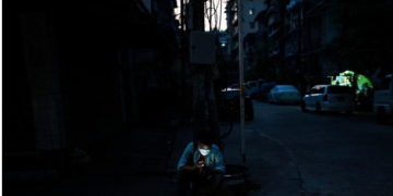 လျှပ်စစ်မီးပျက်နေသည့် ရန်ကုန်မြို့တွင် လမ်းဘေး၌ မိုဘိုင်းဖုန်း သုံးနေသူတဦးကို ၂၀၂၂ ခုနှစ်၊ မတ်လက တွေ့ရစဉ် / AFP