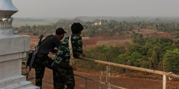 တောင်ကုန်းပေါ်မှနေ၍ ဒီးမော့ဆိုမြို့ကို ကြည့်နေသည့် KNDF မှ တော်လှန်ရေးသမား နှစ်ဦး / Lorcan Lovett